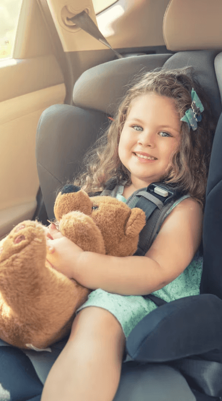 A smiling young child secured in a child safety seat in the back of a car — the legal and safe way to travel with kids in Dubai